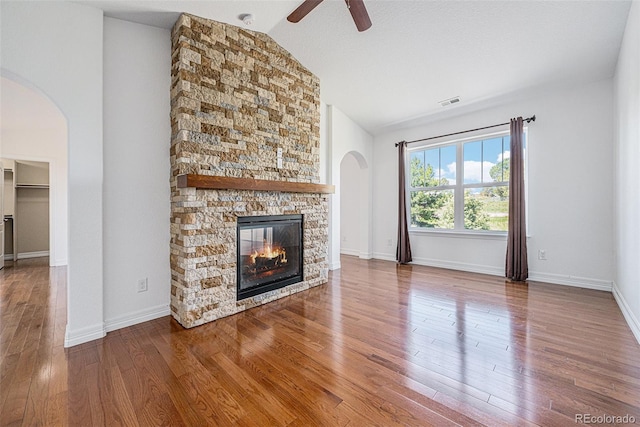 26004 E Elmhurst Pl, Aurora, CO 80016 - unfurnished living room featuring arched walkways, ceiling fan, a fireplace, vaulted ceiling, and wood finished floors