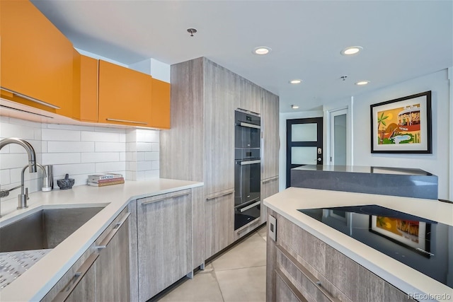 kitchen with light countertops, light tile patterned floors, decorative backsplash, black appliances, and a sink