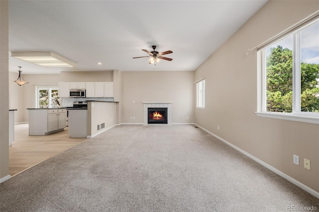 9417 Burgundy Cir, Highlands Ranch, CO 80126 - unfurnished living room featuring light colored carpet, plenty of natural light, a ceiling fan, a tiled fireplace, and recessed lighting