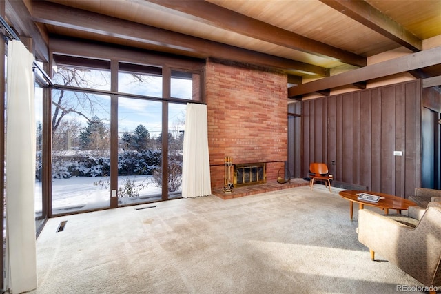 unfurnished living room with a brick fireplace, wooden ceiling, wooden walls, carpet floors, and beamed ceiling