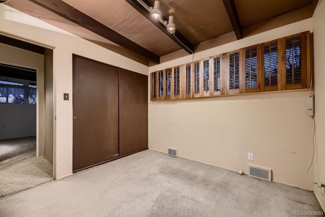 carpeted spare room featuring beamed ceiling and wood ceiling