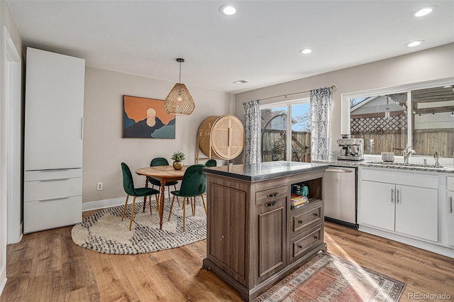 kitchen featuring a sink, light wood-style floors, stainless steel dishwasher, and hanging light fixtures