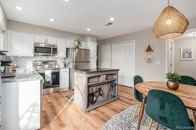 kitchen with decorative light fixtures, white cabinetry, stainless steel appliances, light wood finished floors, and decorative backsplash