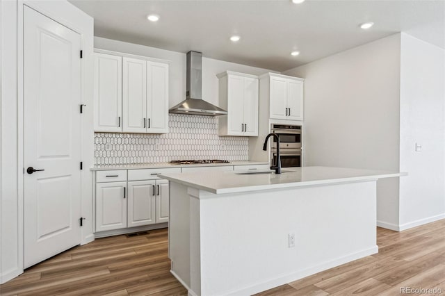 kitchen featuring a kitchen island with sink, wall chimney range hood, white cabinetry, and sink