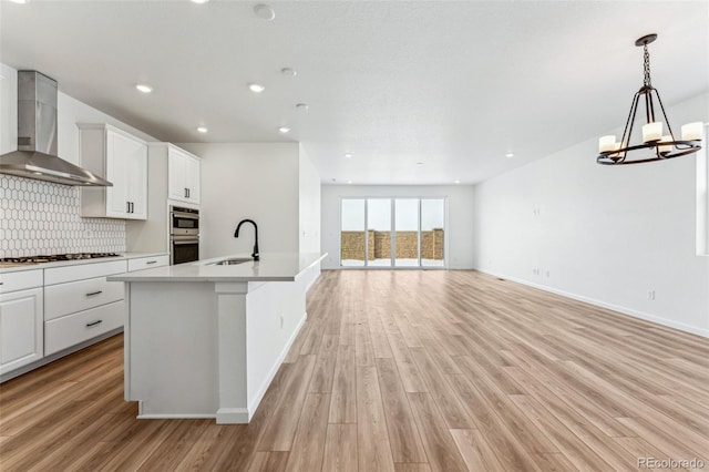 kitchen with sink, stainless steel appliances, white cabinets, a center island with sink, and wall chimney exhaust hood