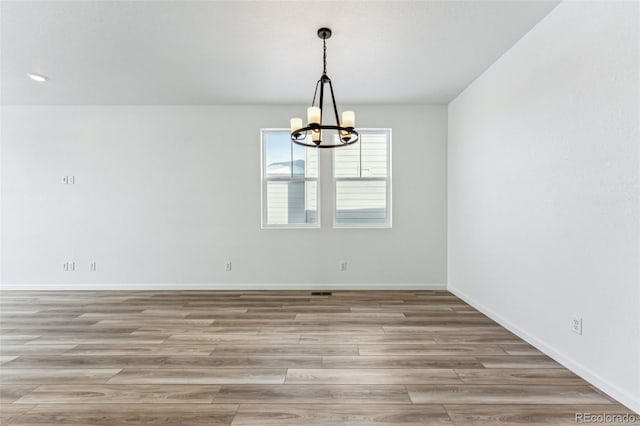 spare room with light hardwood / wood-style floors and a chandelier