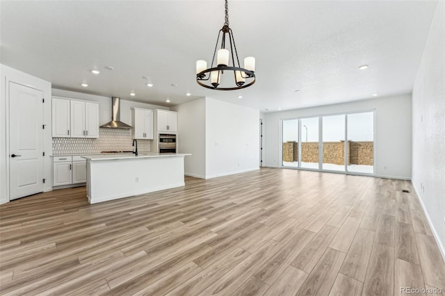 kitchen with pendant lighting, wall chimney range hood, tasteful backsplash, an island with sink, and white cabinets