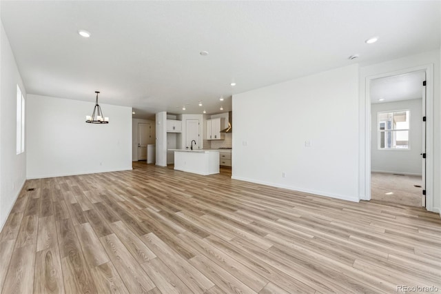 unfurnished living room with sink, an inviting chandelier, and light hardwood / wood-style flooring