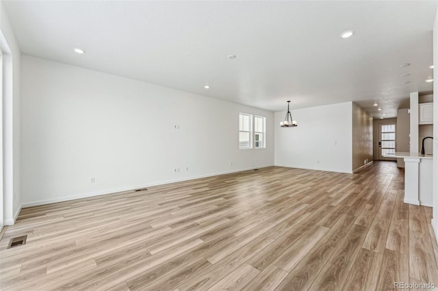 unfurnished living room with a chandelier and light hardwood / wood-style floors