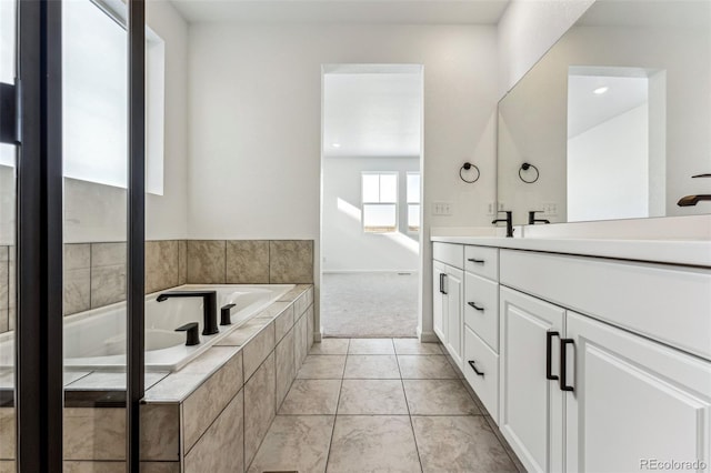 bathroom with a relaxing tiled tub, vanity, and tile patterned floors