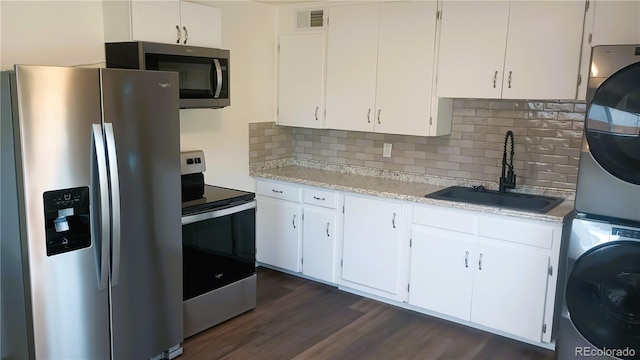 kitchen with appliances with stainless steel finishes, stacked washing maching and dryer, sink, dark hardwood / wood-style floors, and white cabinetry