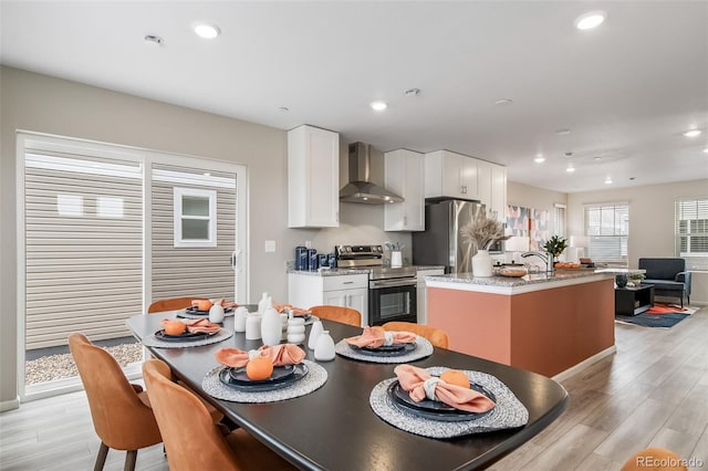 13029 E 103rd Pl, Commerce City, CO 80022 - kitchen featuring stainless steel appliances, wall chimney range hood, a center island with sink, white cabinetry, and light wood-style floors