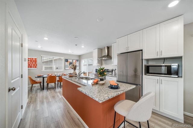 13029 E 103rd Pl, Commerce City, CO 80022 - kitchen with wall chimney range hood, stainless steel appliances, a sink, a kitchen island with sink, and light wood-style flooring