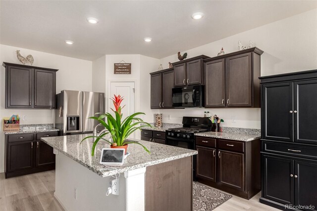 318 Thomas Ave, Keenesburg, CO 80643 - kitchen featuring black appliances, light wood-type flooring, an island with sink, light stone counters, and dark brown cabinets