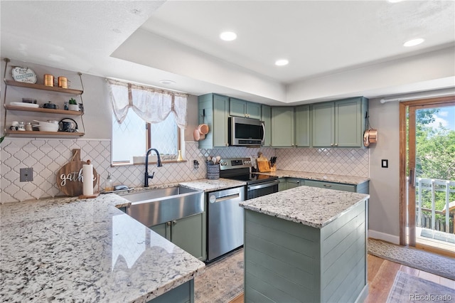 kitchen with green cabinets, appliances with stainless steel finishes, light stone countertops, and sink