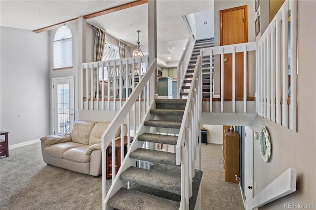 staircase with a towering ceiling, a textured ceiling, and carpet