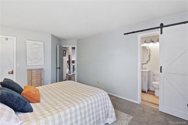 bedroom with carpet flooring, ensuite bathroom, a barn door, and a textured ceiling