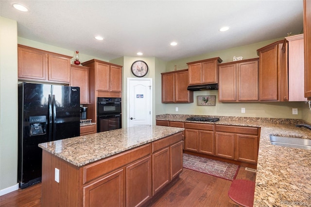 kitchen featuring black appliances, dark hardwood / wood-style flooring, a kitchen island, sink, and light stone countertops