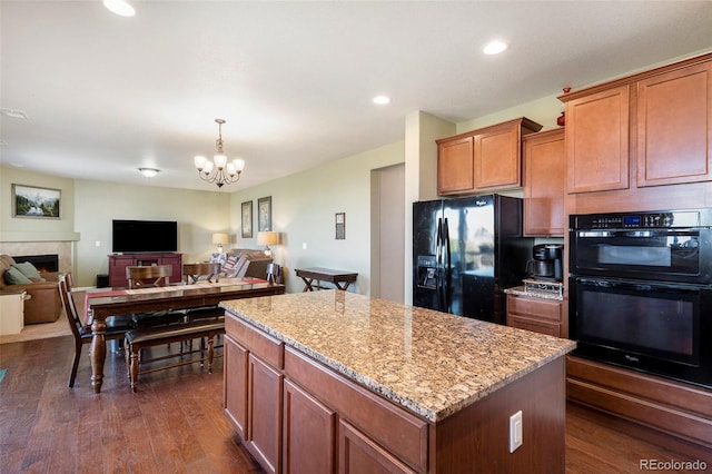 kitchen featuring a kitchen island, an inviting chandelier, black appliances, dark wood-type flooring, and light stone counters