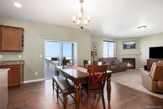 dining room with dark wood-type flooring, a tiled fireplace, and a chandelier