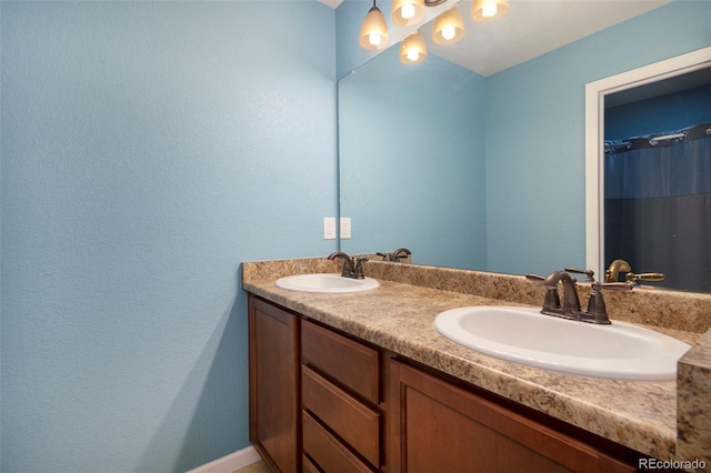 full bath featuring double vanity, a textured wall, and a sink