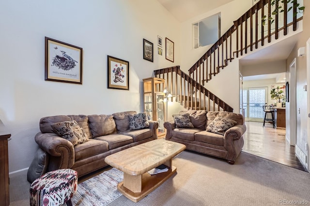 carpeted living room featuring a high ceiling, stairs, baseboards, and a wall unit AC