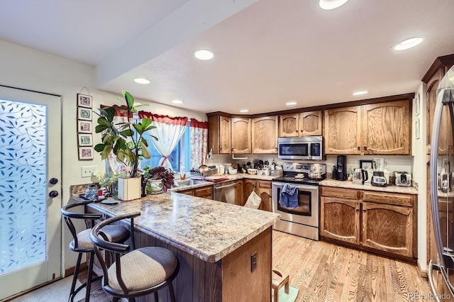 kitchen with stainless steel appliances, a peninsula, a kitchen bar, light countertops, and recessed lighting