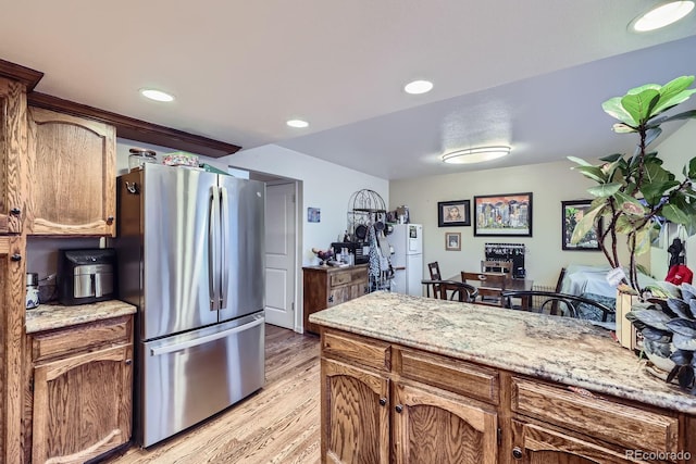 kitchen featuring freestanding refrigerator, light wood-style floors, recessed lighting, light stone counters, and brown cabinets