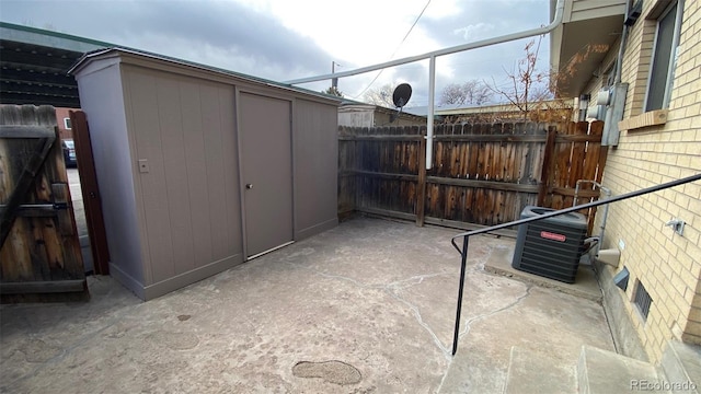 view of patio / terrace featuring an outbuilding, central air condition unit, a storage unit, and fence