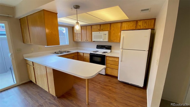 kitchen featuring visible vents, a sink, dark wood finished floors, white appliances, and a peninsula