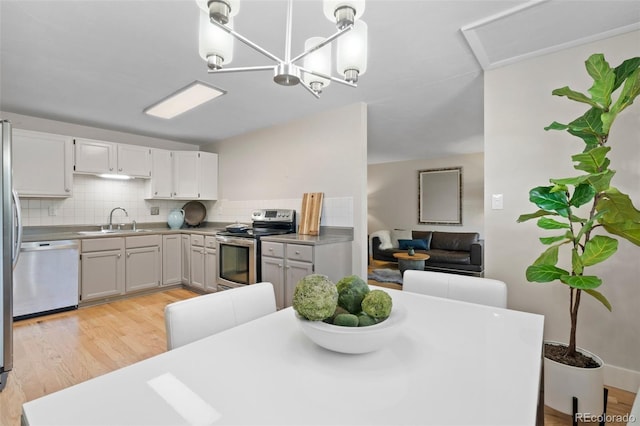kitchen featuring appliances with stainless steel finishes, a sink, light wood finished floors, decorative backsplash, and pendant lighting
