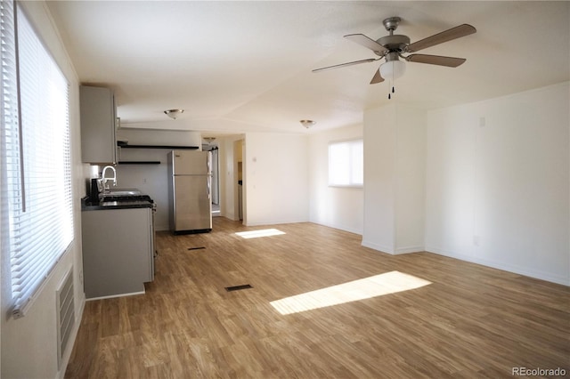 unfurnished living room with a sink, light wood-type flooring, baseboards, visible vents, and ceiling fan