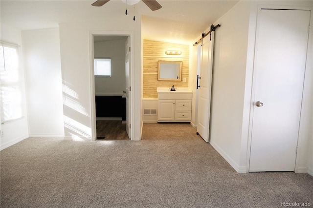 unfurnished bedroom featuring a barn door, visible vents, baseboards, light colored carpet, and ensuite bathroom