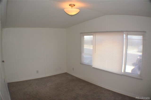 spare room featuring lofted ceiling, dark colored carpet, and baseboards