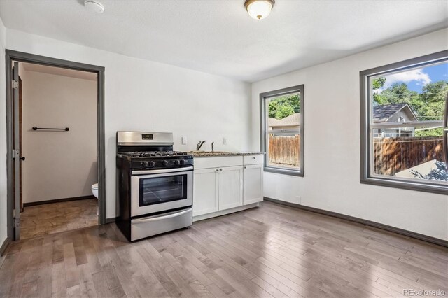 646 Maple St, Colorado Springs, CO 80903 - kitchen featuring stainless steel gas range oven, white cabinetry, light wood-type flooring, and light stone countertops