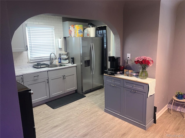 kitchen with tasteful backsplash, sink, gray cabinets, stainless steel fridge with ice dispenser, and light hardwood / wood-style flooring