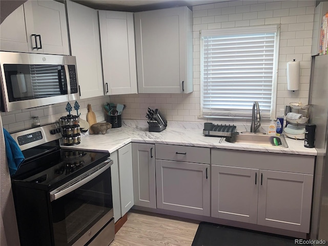 kitchen featuring light hardwood / wood-style floors, appliances with stainless steel finishes, decorative backsplash, light stone counters, and sink