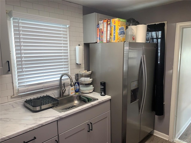 kitchen featuring a healthy amount of sunlight, backsplash, stainless steel fridge, and sink