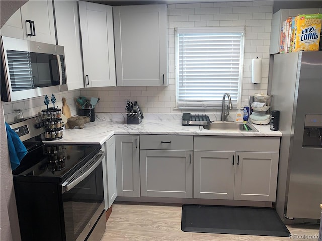 kitchen with backsplash, light hardwood / wood-style floors, sink, stainless steel appliances, and light stone counters