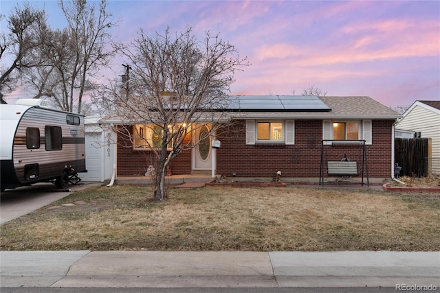 view of front of home featuring roof with shingles, fence, a yard, roof mounted solar panels, and brick siding