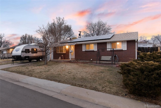 view of front of property with solar panels, brick siding, fence, a lawn, and roof with shingles