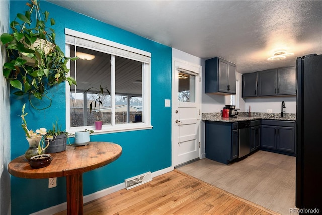 kitchen featuring visible vents, freestanding refrigerator, a sink, dark stone countertops, and light wood-type flooring