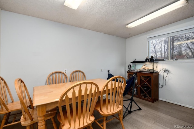 dining area with light wood-style flooring, baseboards, and a textured ceiling