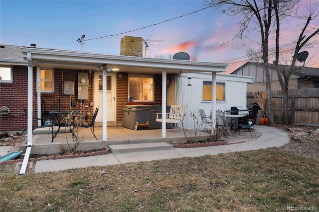 back of property at dusk with brick siding, a patio, a chimney, a hot tub, and fence