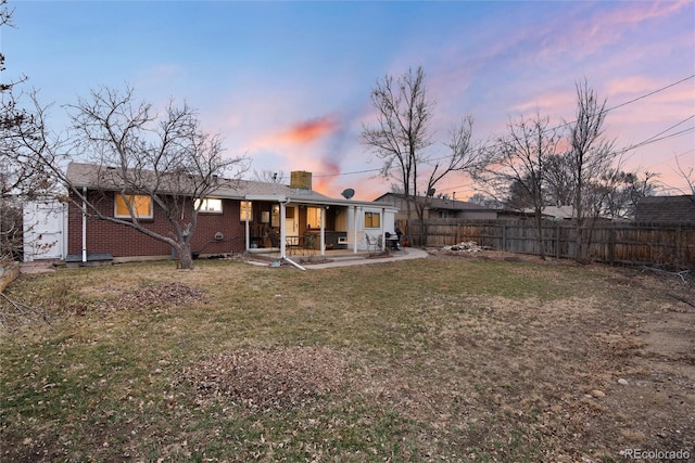 rear view of house with a chimney, fence, a yard, a patio area, and brick siding