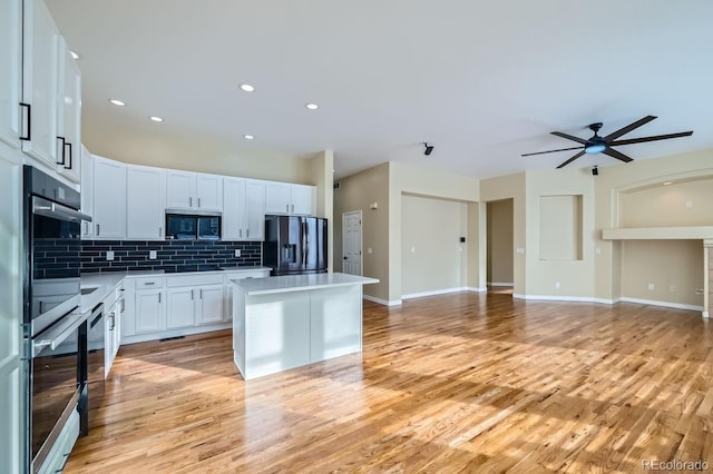 kitchen featuring tasteful backsplash, a kitchen island, open floor plan, stainless steel appliances, and white cabinetry