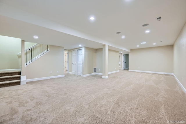 finished basement featuring baseboards, stairway, visible vents, and light colored carpet