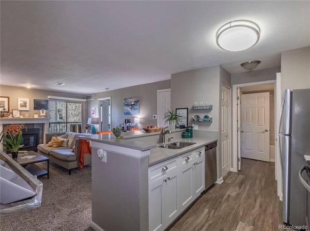 kitchen featuring a sink, open floor plan, white cabinets, a peninsula, and appliances with stainless steel finishes
