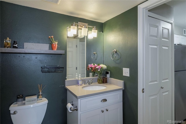 half bathroom featuring a textured wall, visible vents, toilet, and vanity