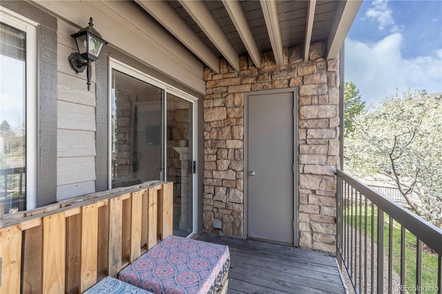 view of exterior entry featuring stone siding and a balcony